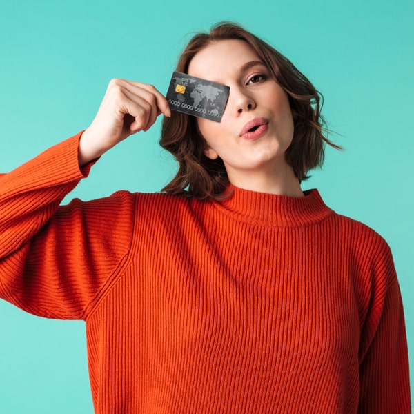 Person wearing an orange sweater holds a credit card, symbolizing the benefits of a high credit score for financial well-being and access to credit.