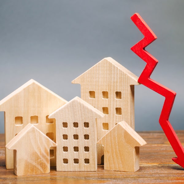Wooden cutouts of buildings with a red arrow depicting financial decline, illustrating the benefits of maintaining a high credit score to avoid negative financial impacts.